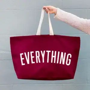 A hand holding a maroon tote bag with the word Everything on it in white