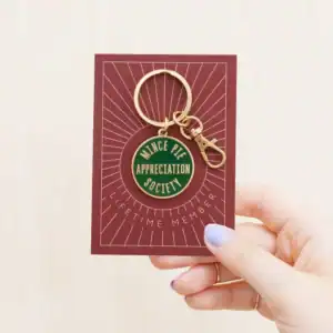 A green and gold keyring on a piece of maroon card being held