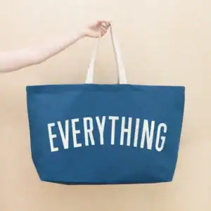 A hand holding a blue oversized tote that says Everything.